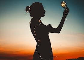 Artistic silhouette of a woman wrapped in fairy lights during a vibrant sunset.
